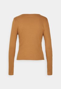 Pitkähiha, istuva paita ruskeasta ribbikankaasta, jossa on pyöreä kaula-aukko ja minimaaliset saumat. Paita on sileäntuntuinen ja sen siluetti on muotoiltu.