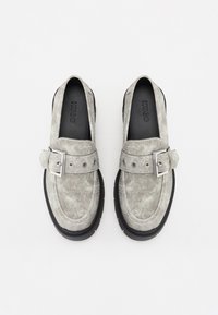 Grå ruskinds loafers med en bred rem og sølvspænde, der har en tekstureret overflade og en tyk sort gummisål.