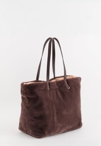 Sac fourre-tout en fausse fourrure marron avec une texture pelucheuse, doté de longues anses marron et d'une doublure beige douce. Design simple et rectangulaire.