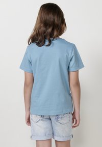 Camiseta de algodón de color azul claro con mangas cortas, escote redondo y detalle de costura en la parte posterior, combinada con pantalones cortos de mezclilla de color claro.