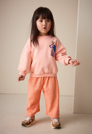 Bluză roz cu mâneci bufante, decorată cu un design colorat cu câine, asortată cu pantaloni largi portocalii cu carouri și adidași cu modele.