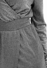 Top cruzado de color gris plateado que presenta mangas largas, textura acanalada y una cinturilla elástica con detalles fruncidos en la cintura.