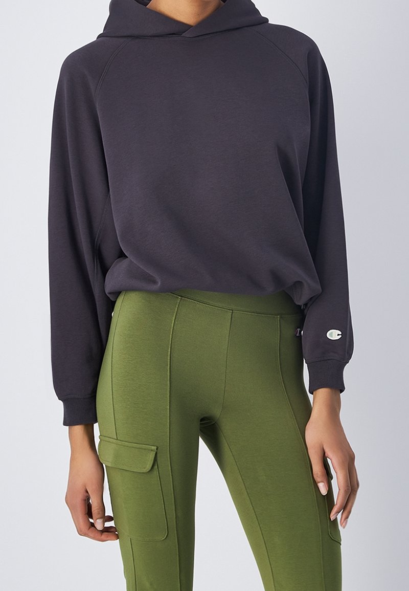 Sudadera con capucha gris oscuro y mangas raglán, combinada con leggings de tiro alto en verde oliva que tienen bolsillos tipo cargo. Ambos artículos están hechos de una tela suave.