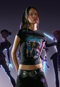 Czarny t-shirt z kolorowym nadrukiem przedstawiającym trzy postacie. Połączony z czarnym paskiem ozdobionym sercowatymi klamrami.