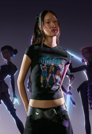 Zwart T-shirt met een kleurrijke grafische print van drie karakters. Gecombineerd met een zwarte riem met hartvormige gespen.