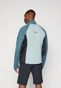 Jachetă ușoară cu o combinație de culori teal și negru. Textură matlasată pe spate, partea din față cu fermoar și un design sportiv.