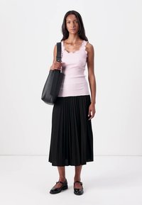 Débardeur rose clair à rayures avec un col festonné, assorti à une jupe plissée noire. Sac épaule noir, chaussures noires à bout rond.