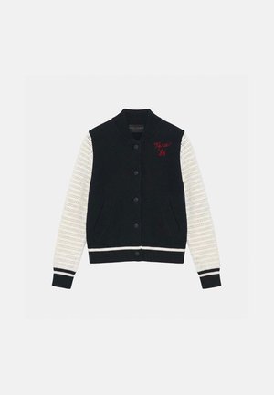 Veste universitaire tricotée en noir et blanc avec fermeture à boutons, col et poignets côtelés, et broderie rouge "Tara '86" sur la poitrine.