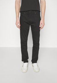 Jeans in denim nero con una vestibilità slim, cinque tasche e cuciture a contrasto. Abbinati a sneakers bianche e una t-shirt nera.