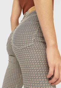 Hondstooth-gepatroneerde leggings in zwart, wit en roestkleur. Rekbare stof met een middelhoge taille en achterzakken. Leren patch op de tailleband.