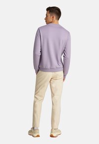 Ανοιχτό μωβ φούτερ με στρογγυλή λαιμόκοψη, ριμπ μανίκια και στρίφωμα, συνδυασμένο με μπεζ παντελόνι και μπεζ αθλητικά παπούτσια.