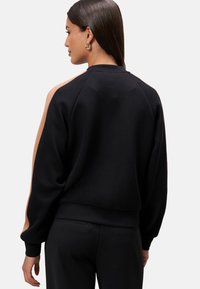 Black sweatshirt with raglan sleeves, featuring a tan accent along the shoulders. Made of soft fabric, with a relaxed fit and crew neckline.