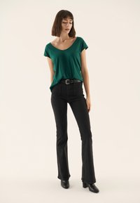 Roheline lühikese varrukaga V-kaelusega T-särk, millel on kõrge vöökohaga mustad laugjas püksid ja mustad pahkluu saapad. Sile kangas ja mugav lõige.