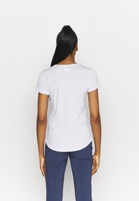 Bílý krátký rukáv tričko s kulatým výstřihem a zakřiveným lemem. Má malé logo na horní části zad. Hladký materiál.