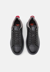 Par av svarta lädersnörskor med grå vadderade kragar, röda hältappar och "HUGO"-logotyp på tungan och innersulorna.