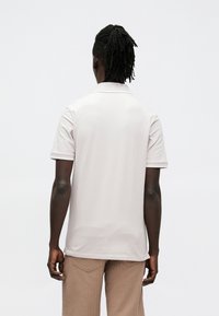 Lichtroze poloshirt met korte mouwen en een kraag. Gladde textuur, effen ontwerp, en subtiel geribbelde details langs de halslijn en mouwen.