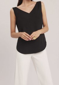 Top negro sin mangas con escote en V y dobladillo curvado, hecho de tela suave. Combinado con pantalones anchos blancos y un anillo dorado.