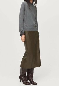 Pull gris à manches longues, associé à une jupe en cuir vert olive foncé et des bottes bordeaux montantes, créant une tenue superposée et texturée.