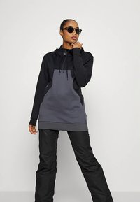 Bluza z kapturem w kolorze czarno-szarym, z kieszenią kangurką i sznurkiem do regulacji. Połączona z czarnymi spodniami i okularami przeciwsłonecznymi. Gładka faktura.