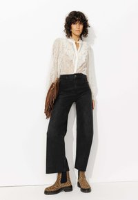 Blouse en dentelle blanche avec un col à volants, jeans noirs à taille haute et jambes évasées, et bottines chevilles en imprimé léopard marron. Sac à franges marron.