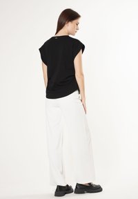 Top negro de manga corta con un ajuste relajado, combinado con pantalones anchos blancos y mocasines negros de suela gruesa. El fondo es blanco liso.