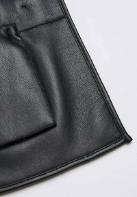 Assise de chaise en cuir noir texturé avec coussin cousu et bords arrondis passepoilés sur fond clair.