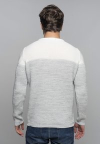 Pull en maille gris clair avec un empiècement texturé blanc. Il présente des manches longues et un col rond, fabriqué à partir d'un matériau doux et confortable.
