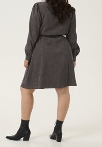 Grijze corduroy jurk met lange pofmouwen, een aangesnoerde taille en een uitlopende rok, gecombineerd met zwarte enkelboots. Glad textuur en subtiele glans.