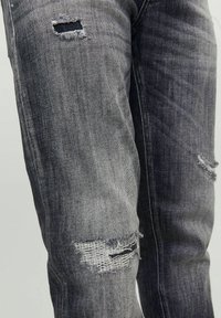Svarta denimjeans med slitna lappar. Har revna knäpartier, fransiga kanter och en blekt tvätt, vilket framhäver struktur och slitage.