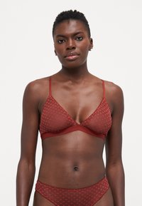 Rød, gjennomsiktig trekantet bralette med prikkete mønster, tynne stropper og blondedetaljer. Sammen med matchende truser. Mykt stoff og tettsittende design.