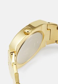 Orologio da polso dorato con cassa rettangolare, corona testurizzata e bracciale metallico. Retro liscio con dettagli incisi e maglie.