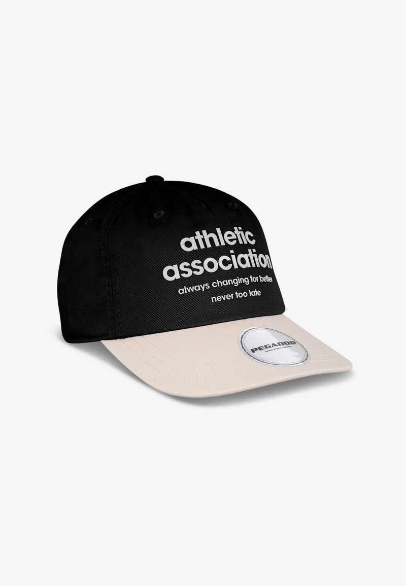 Casquette de baseball noire avec une visière crème. Présente un texte blanc : "association athlétique toujours en train d'évoluer pour le mieux, jamais trop tard." Étiquette de logo rond attachée.