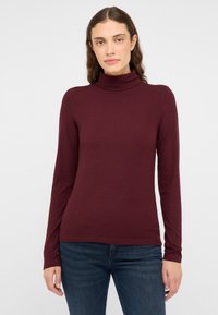 Bordowa bluzka z długim rękawem i golfem o prążkowanej teksturze, dopasowany fason, miękki materiał, w połączeniu z ciemnoniebieskimi dżinsami. Prosta i uniwersalna.