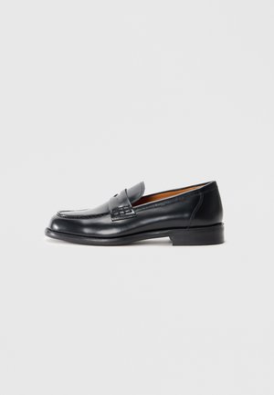 Black leather loafer with a rounded toe, stitched detailing, and a smooth texture. Features a low heel and slip-on design.
