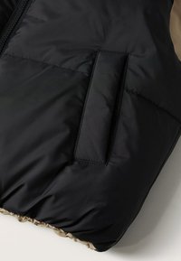 Gros plan d'une poche de veste matelassée noire avec une fente verticale et des coutures détaillées le long des bords.