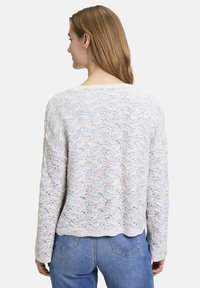 Lätt, flerfärgad stickad tröja med ett vågmönster, rund halsringning och ribbade muddar, matchad med blå denimjeans.