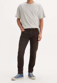 T-shirt in cotone grigia con un piccolo logo Levi's, abbinata a jeans marrone scuro e sneakers in tela blu con suole e lacci bianchi.