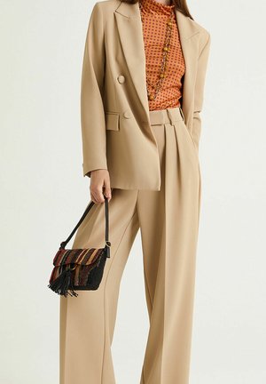 Beige tailored suit with wide-leg trousers and a double-breasted blazer, paired with a textured, multicolored striped handbag and polka-dot top.