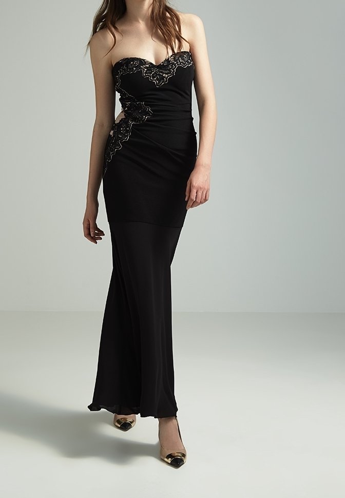 Svart axelbandslös aftonklänning med en figurnära silhuett, rynkat mönster och intrikata spetsdetaljer med gulddetaljer. Golvlång.