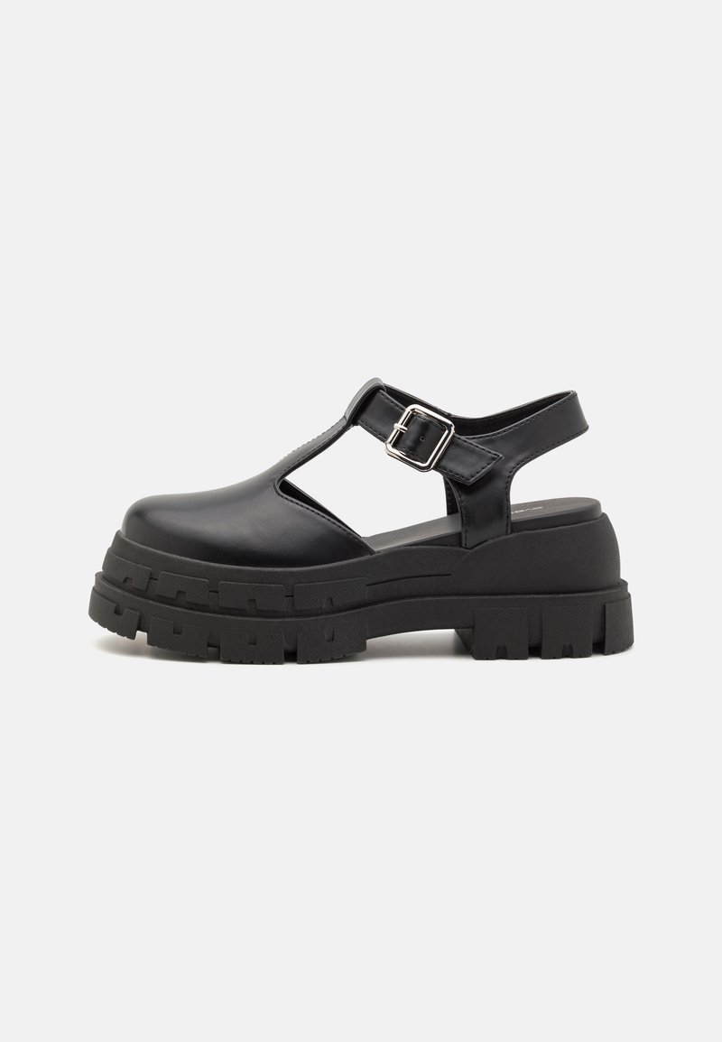 Black platform sandals made of smooth synthetic material, featuring an open toe, cut-out design, adjustable buckle, and thick, textured sole.