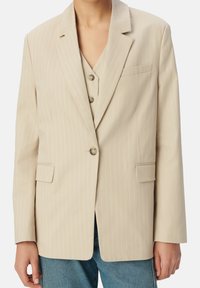 Blazer beige a righe con un design strutturato, revers a punta, una tasca sul petto, due tasche frontali e chiusura a due bottoni.