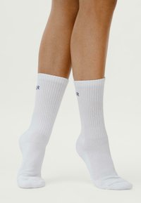 Calzini bianchi in cotone con texture a coste, dotati di un logo a contrasto in blu navy. Il design include una lunghezza standard e punta senza cuciture.