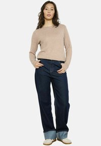 Maglione beige, texture con maniche lunghe, abbinato a jeans a gamba larga blu scuro con fondo risvolto e scarpe crema.