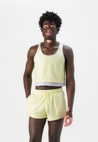 Limegrønn mesh tanktop med lys grå kant og matchende shorts. Tøyet har en perforert tekstur og elastisk midjebånd.