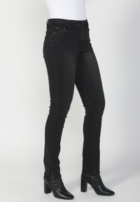 Jeans ajustados negros de mezclilla, con un talle medio, bolsillos frontales y aberturas en el dobladillo. Llevados con botas negras de tacón alto.