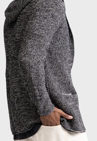 Cardigan lavorato a maglia con cappuccio in tessuto mélange bianco e nero, caratterizzato da una tasca laterale e un design aperto davanti.