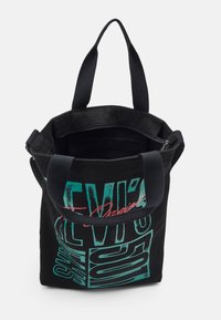 Zwarte canvas schoudertas met grafische afdruk in teal en rood. Beschikt over dubbele hengsels en een ritsvak aan de binnenzijde. Ruim ontwerp met een open bovenkant.