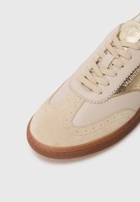 Sneaker in suede e pelle beige con dettagli perforati, lacci piatti beige e suola in gomma color caramello; presenta un dettaglio con logo dorato.