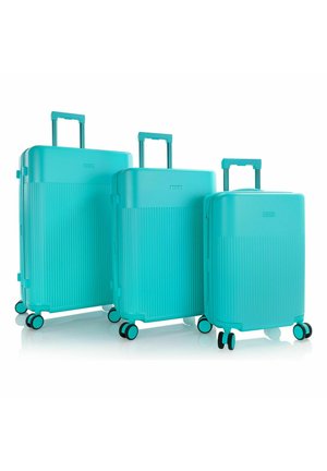 Trois valises rigides turquoises avec poignées télescopiques et quatre roues pivotantes, disposées de la plus grande à la plus petite sur un fond blanc.