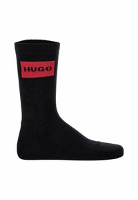 Sort bomuldsstrømpe med ribbet tekstur og en rød rektangulær logo-patch med ordet "HUGO" i sort.